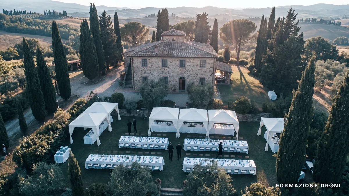 Veduta aerea di una villa di campagna con giardino allestito per un ricevimento fra i cipressi