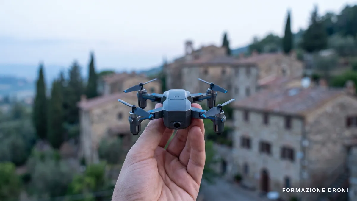 Un piccolo drone pieghevole appoggiato sul palmo di una mano, con colline italiane sullo sfondo