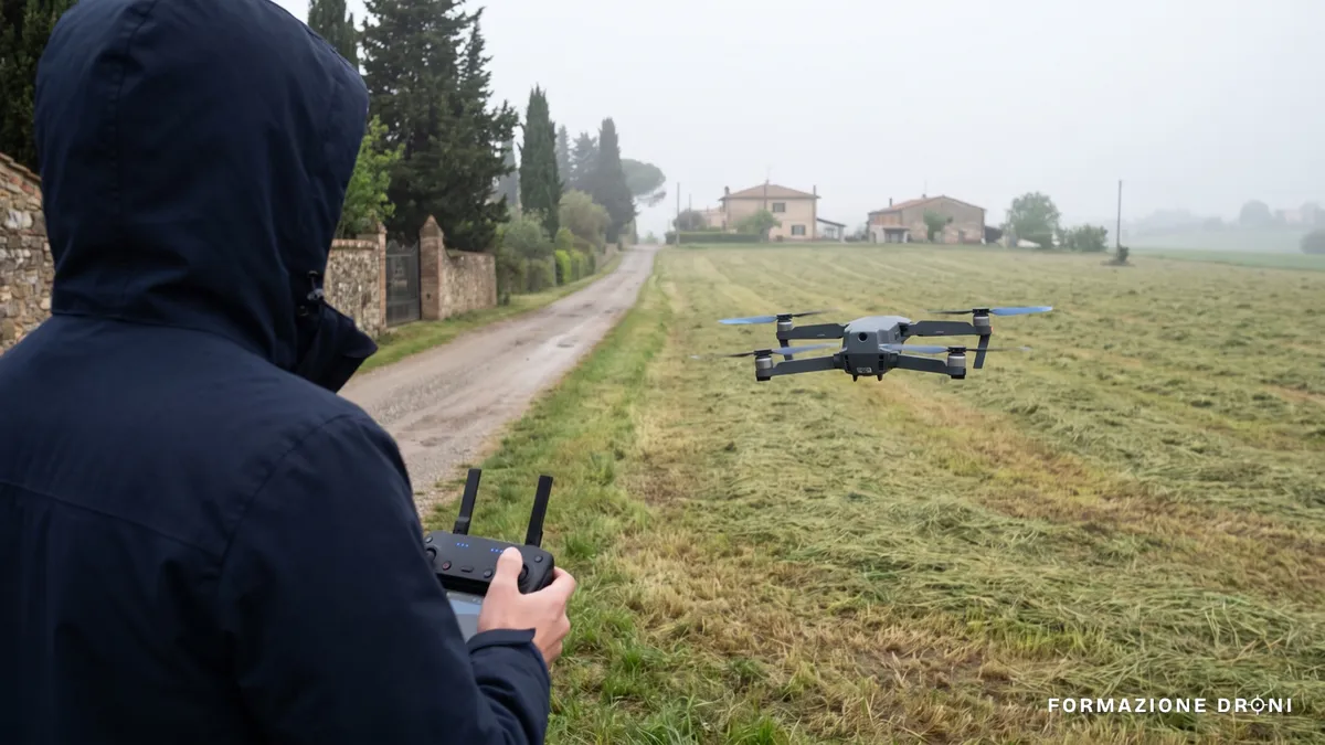 Drone consumer in volo basso su un prato, con un pilota di spalle che tiene il radiocomando