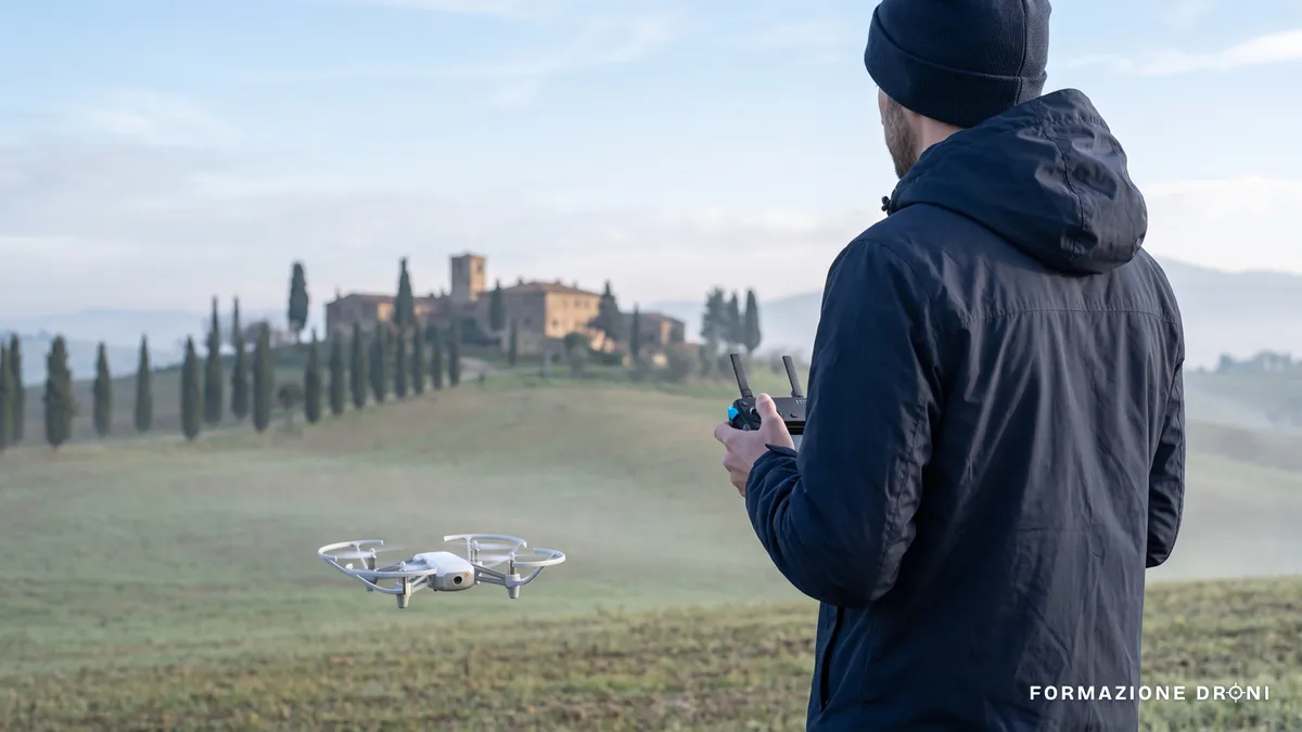 Pilota di spalle con radiocomando e piccolo drone in volo basso sopra una campagna italiana