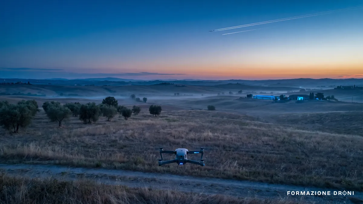 Drone in volo basso su una pianura italiana con scie di aerei di linea in alta quota