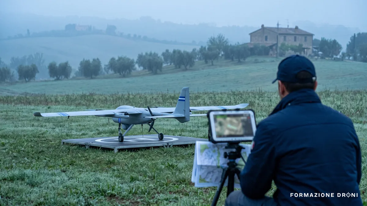 Drone VTOL ad ala fissa pronto al decollo su un campo con un tecnico che prepara la stazione di controllo